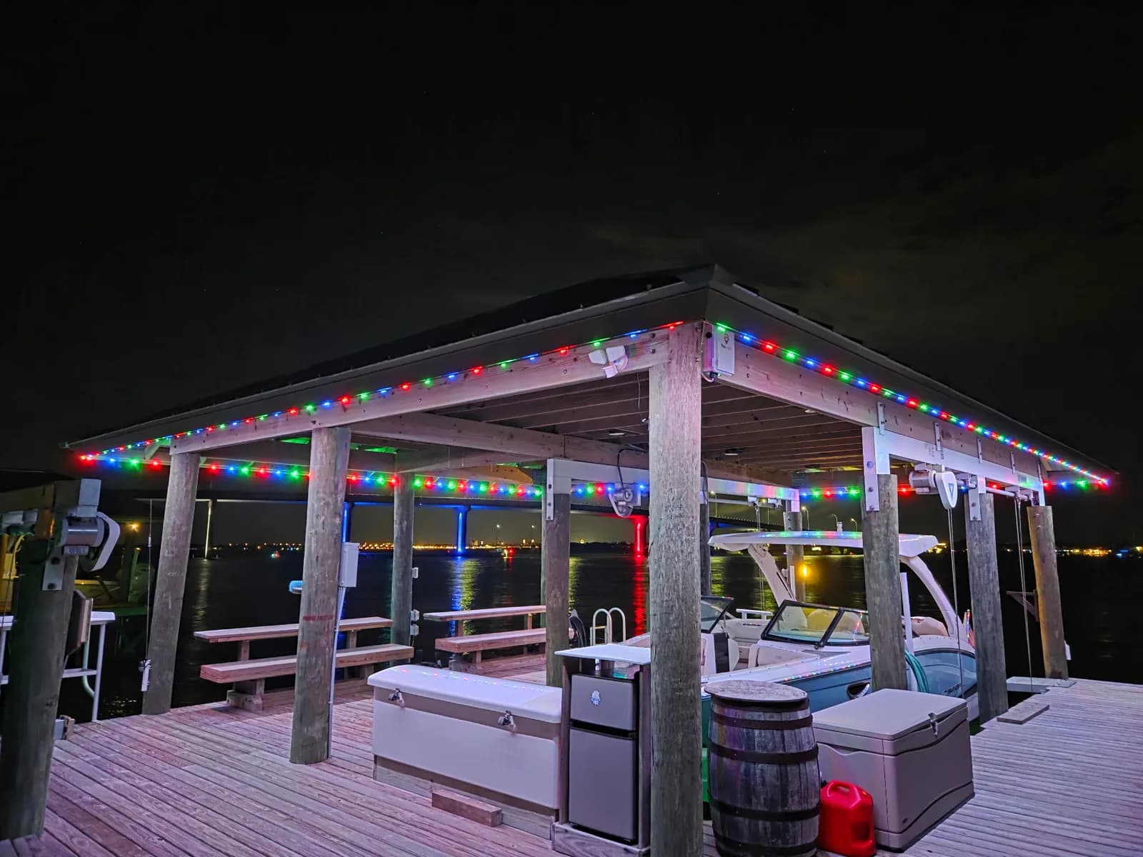 Covered boat dock in St. Augustine at night with red, green and blue permanent lighting along the roofline and a boat below.