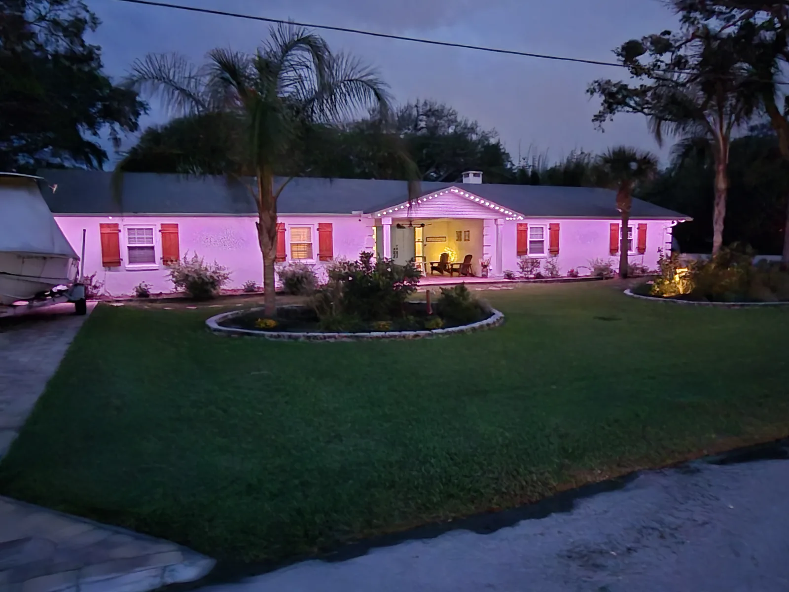 Single-story St. Augustine home with light purple permanent roofline lighting at dusk, palm trees in the front yard.